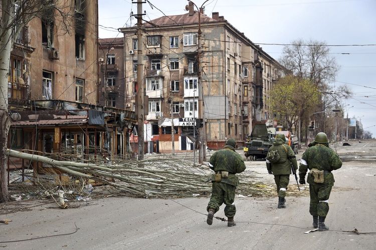 Prajurit milisi Republik Rakyat Donetsk berjalan melewati bangunan apartemen yang rusak di dekat Pabrik Metalurgi Illich Iron & Steel Works, perusahaan metalurgi terbesar kedua di Ukraina, di daerah yang dikendalikan oleh pasukan separatis yang didukung Rusia di Mariupol, Ukraina, Sabtu, 16 April 2022.