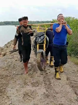 Petugas Damkar Sumenep menandu motor melewati jalan berlumpur dan licin. 