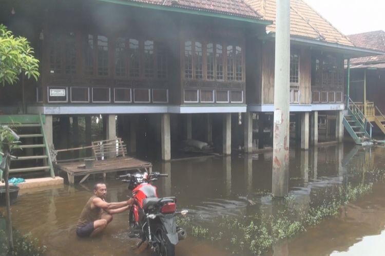 Warga Desa Tanjug Dayang Ogan Ilir memanfaatkan air banjir yang menggenagi halaman rumahnya untuk mencuci sepeda motor