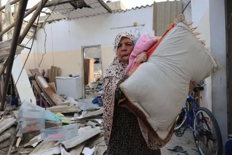 Seorang perempuan Palestina menyelematkan sejumlah barang dari rumahnya yang hancur akibat serangan udara Israel di Rafah, bagian selatan Jalur Gaza, pada 8 Oktober 2023. 