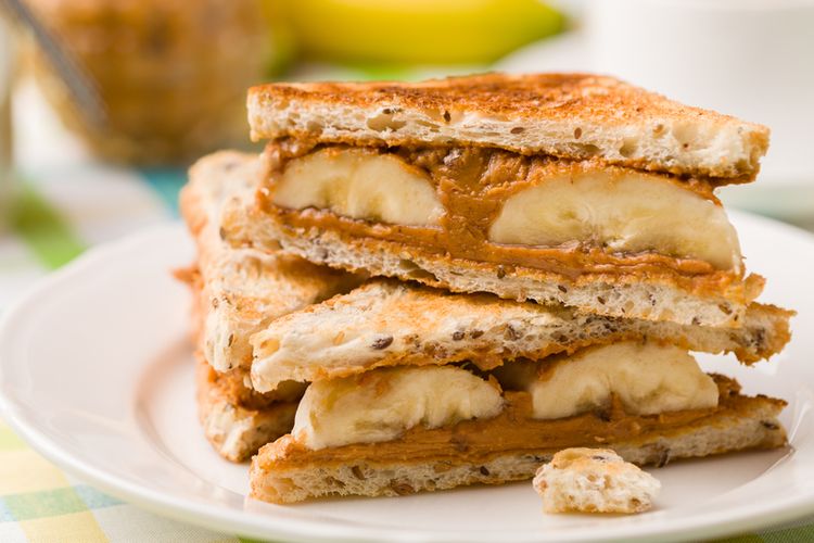 Seporsi sandwich pisang dengan selai kacang, madu, dan roti gandum yang siap dinikmati sebagai sarapan sehat atau cemilan sore yang lezat