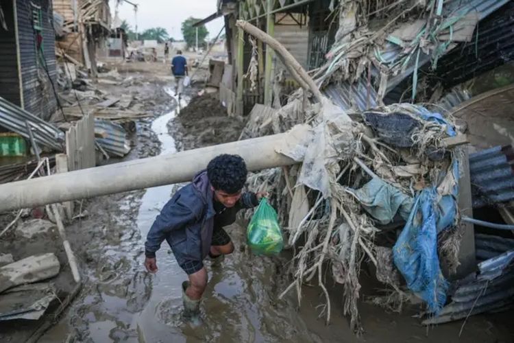 Warga merunduk melewati tiang listrik yang roboh akibat banjir bandang di Kuala Simpang, Kabupaten Aceh Tamiang, Aceh, Sabtu (6/12/2025).