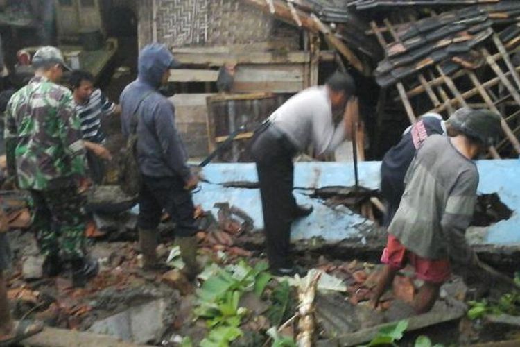 Anggota Polsek Sine bersama warga setempat membersihkan reruntuhan material tembok yang menimpa rumah seorang petani bernama  Rismanto (50), warga Dusun Krajan, Desa Kuniran, Kecamatan Sine, Kabupaten Ngawi, Selasa (14/2/2017) sore. 