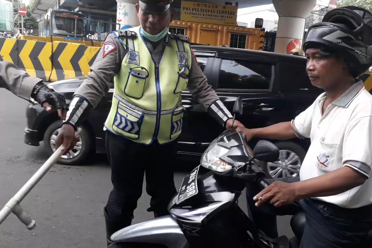 Seorang pengendara motor dihentikan polisi karena kedapatan merokok saat berkendara di kawasan Kampung Melayu, Senin (8/4/2019).