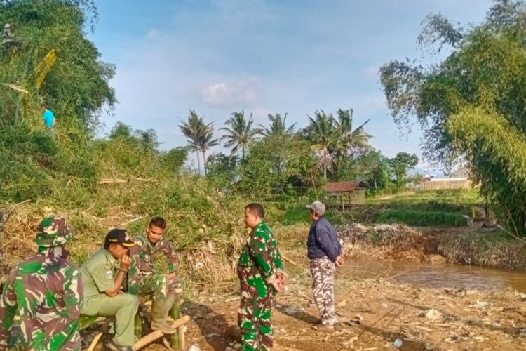 Kepala Desa Suka Senang Iwan Ridwan bersama anggota TNI tampak membersihkan sisa-sisa pepohonan bambu yang menyeret jembatan gantung yang dibangun dan diresmikan Gubernur Jawa Barat yang roboh akibat meluapnya Sungai Cimanuk, Senin (18/07/2022)