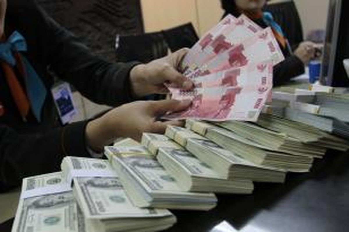 Teller sebuah bank di Jakarta Selatan menghitung uang rupiah di atas dolar Amerika Serikat, Jumat (24/1/2014). 