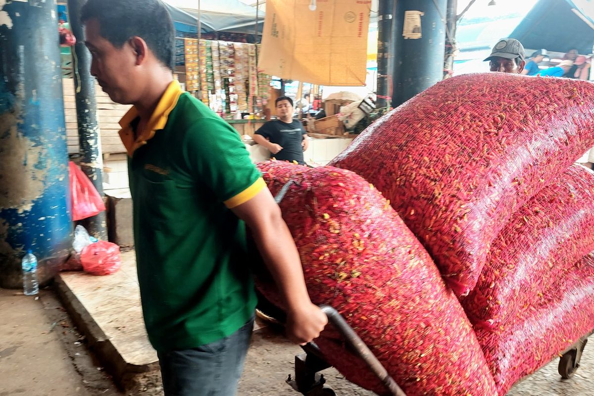 Seorang pedagang tengah membawa karungan cabai merah dari truk pengangkut menuju lapak dagangnya di Pasar Induk Kramat Jati, Jakarta Timur, Selasa (6/12/2022).