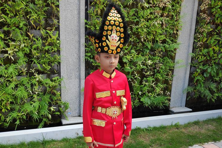 Aditya Perpatih (9) siswa SD yang viral karena menghiasi uang pecahan Rp75000. ia mengenakan baju adat kebesaran kerajaan Gorontalo (Makuta) warna merah.