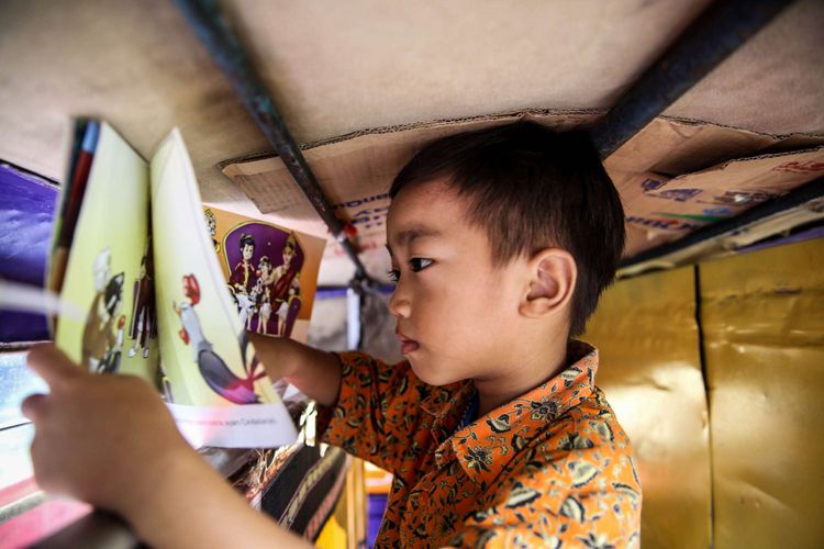 Anak-anak sekolah Paud saat membaca buku di bemo perpustakaan saat jam istirahat di Rusun Karet Tengsin, Jakarta, Jumat (7/12/2018). Pak Sutino (58) adalah sopir bemo yang merintis bemo tuanya menjadi perpustakaan keliling bagi anak-anak sejak tahun 2013.