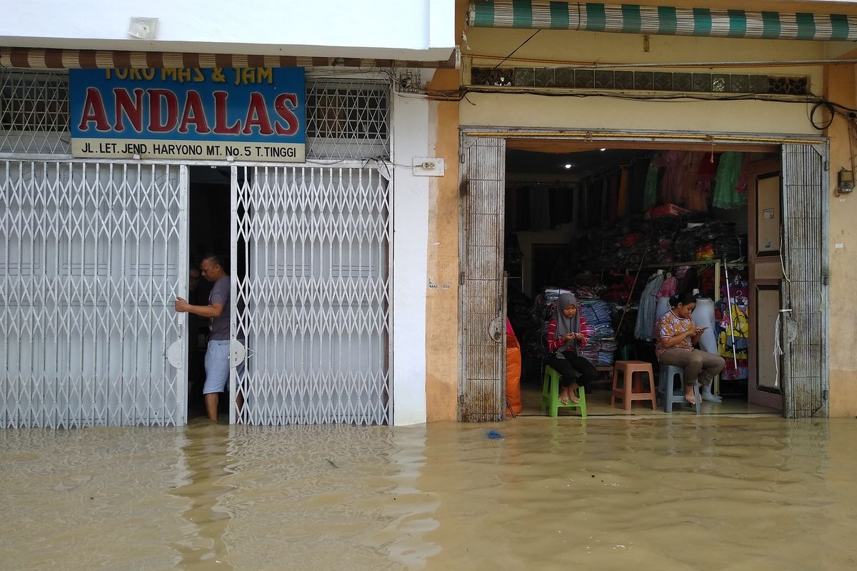 Seorang pria menutup pintu tokonya di Jalan Jend. MT Haryono, Tebing Tinggi, Senin (16/12/2019). Daerah pertokoan ini kebanjiran karena meluapnya Sungai Bahilang sejak dini hari.