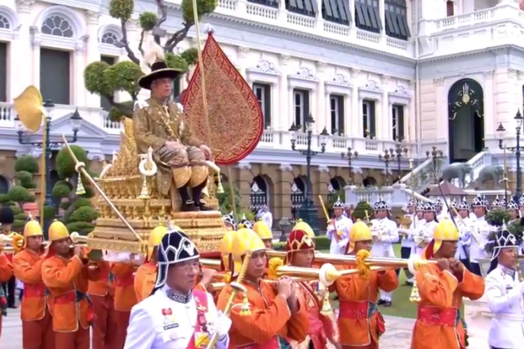 Raja Thailand Maha Vajiralongkorn duduk di atas tandu kerajaan berwarna emas yang diangkat oleh pasukan berseragam oranye dalam perjalanan menuju Kuil Emerald Buddha di Bangkok setelah dinobatkan pada Sabtu (4/5/2019).