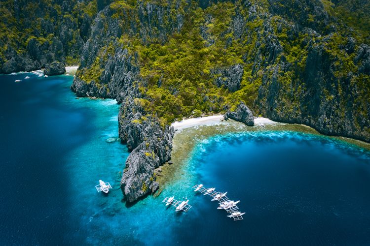 Pemandangan udara Pulau Miniloc, El Nido, Palawan, Filipina dengan perahu selam di atas terumbu karang yang dikelilingi oleh tebing gunung berbatu kapur karst. Wisata bahari di Filipina menjadi salah satu daya tarik bagi wisatawan asing.