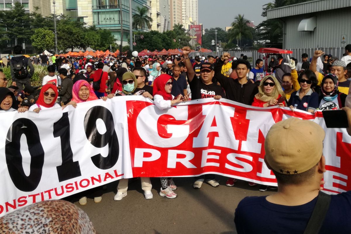 Sejumlah warga tampak berjalan kaki dengan spanduk sembari memakai kaus dan kaus #2019GantiPresiden di Bundaran HI, Jakarta, Minggu (29/4/2018).