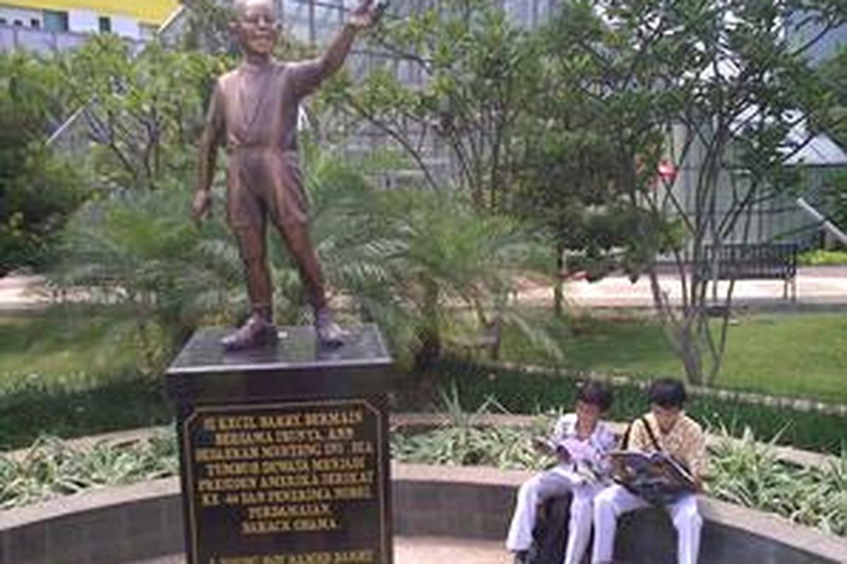 Inilah patung Barrack Obama di Taman Menteng, Jakarta Pusat. Tampak dua orang anak sekolah dasar sedang membaca di dekat patung tersebut.