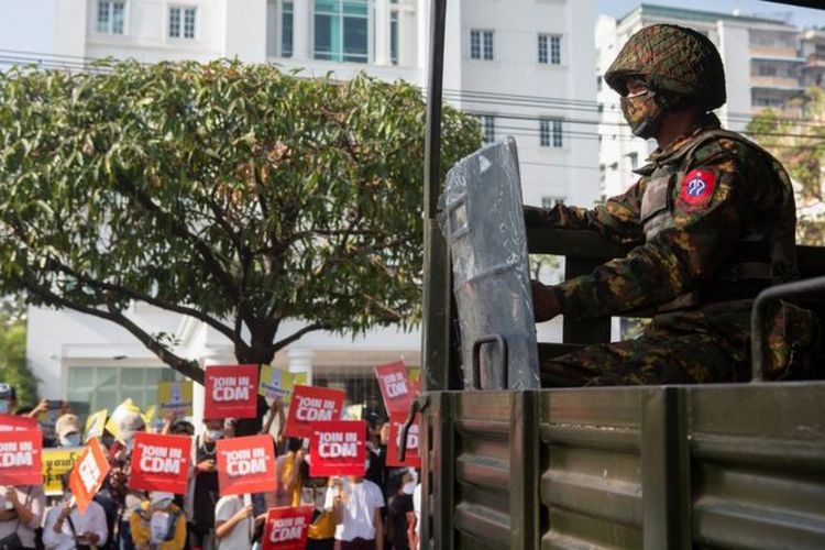 Para pengunjuk rasa membawa plakat Join in CDM, merujuk pada gerakan pembangkangan sipil, di depan kendaraan militer di Yangon, Myanmar.