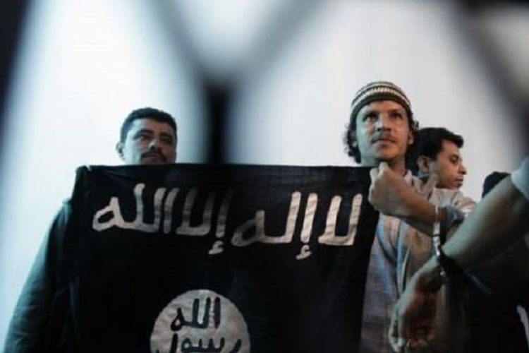 Dalam foto dokumentasi dari tahun 2013 ini, seorang yang diduga sebagai militan Al Qaeda di Yaman, tengah, membentangkan bendera kelompok ISIS di tengah berlangsungnya sebuah persidangan di Sana'a, Yaman. Dalam persaingannya dengan kelompok Negara Islam (ISIS) di Timur Tengah, Al Qaeda menggunakan pendekatan yang dianggap sebagian kalangan sebagai pragmatis.