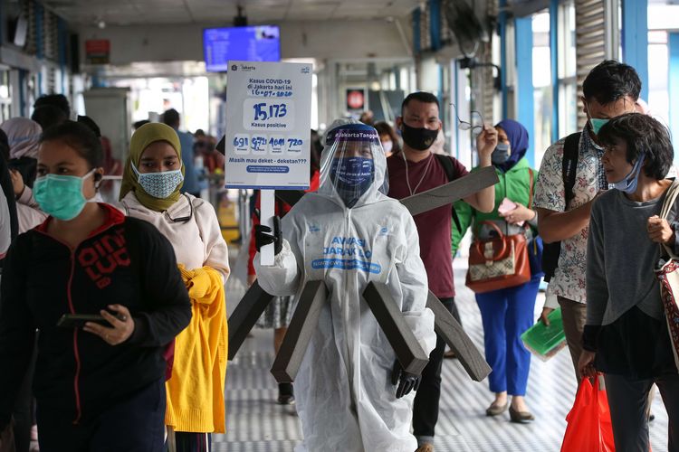 Maskot Manusia Covid membawa poster bertulisakan data penderita Covid-19 terlihat di Halte Transjakarta Harmoni, Kamis (16/7/2020). Maskot Manusia Covid bertujuan mengingatkan penumpang Transjakarta untuk disiplin mematuhi prosedur kesehatan selama masa PSBB Transisi Tahap II berlangsung.