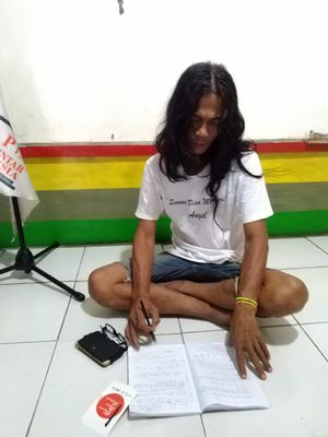 Teguh Suprobo sedang duduk sambil menulis materi yang akan diajarkan kepada anak didiknya.