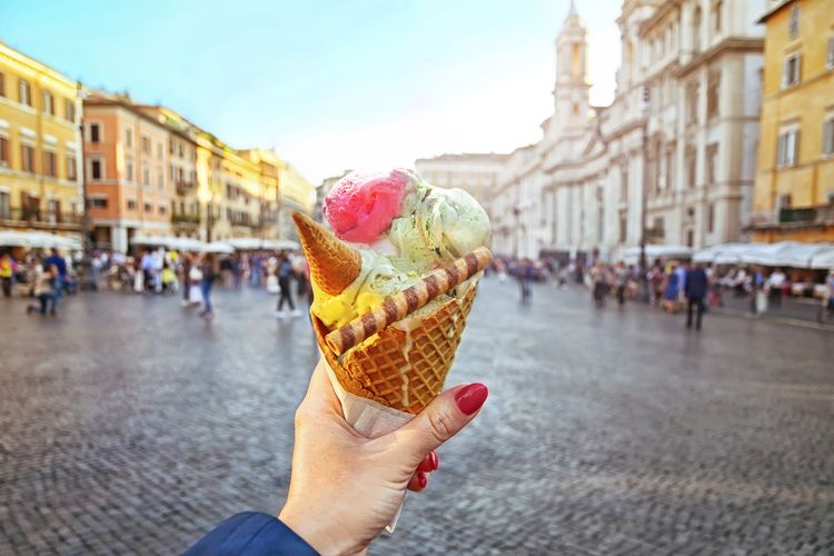 Ilustrasi seseorang memegang gelato dengan latar belakang Piazza Navona di Roma, Italia. 