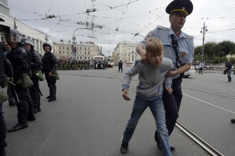 Polisi Rusia mengamankan seorang bocah laki-laki selama unjuk rasa menentang rencana peningkatan usia pensiun nasional di Saint Petersburg, Rusia, Minggu (9/9/2018). (AFP/Olga Maltseva)
