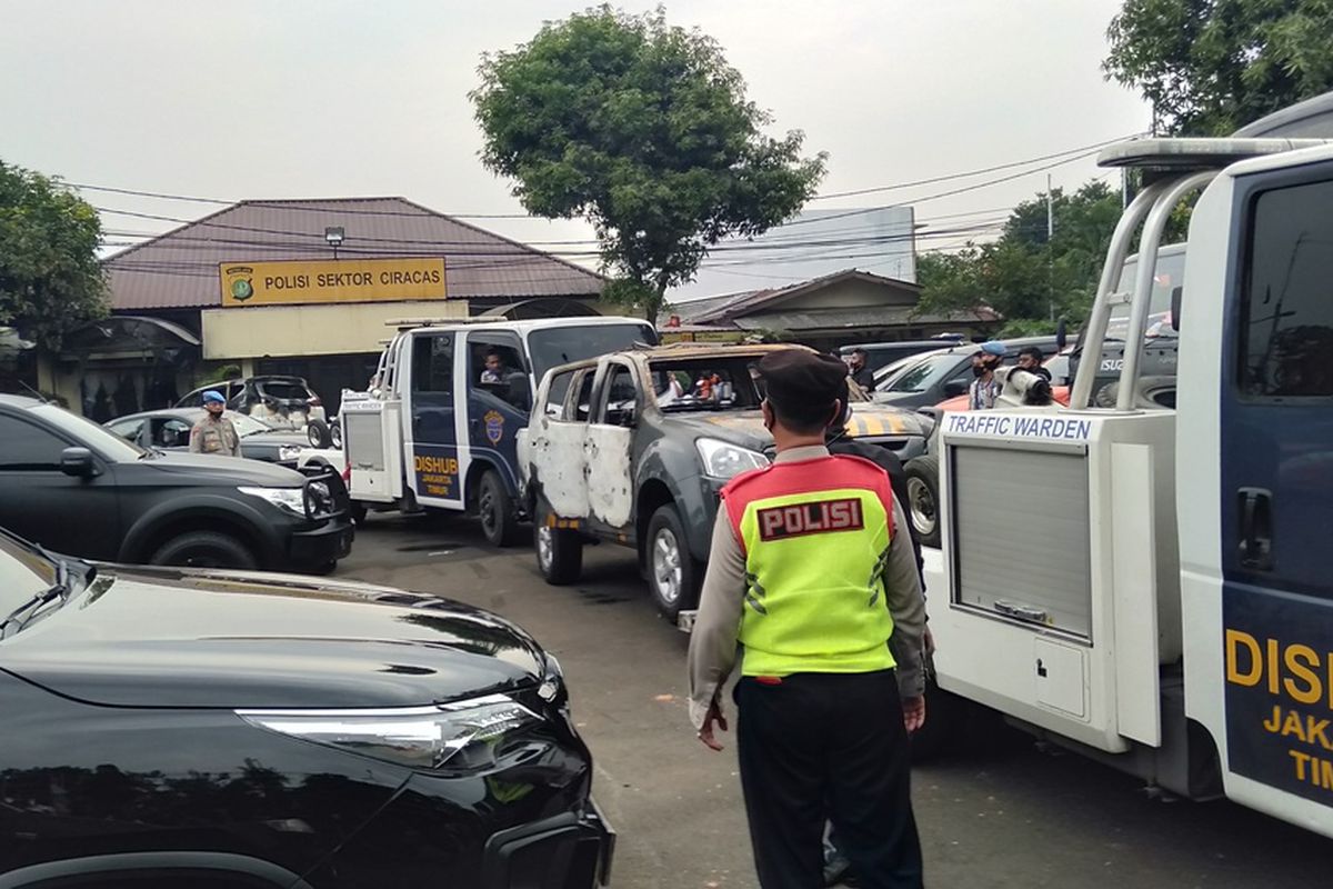 Petugas menderek dua mobil yang terbakar, dua mobil dalam kondisi pecah kaca dan satu bus operasional di Mapolsek Ciracas,  Sabtu (29/9/2020)