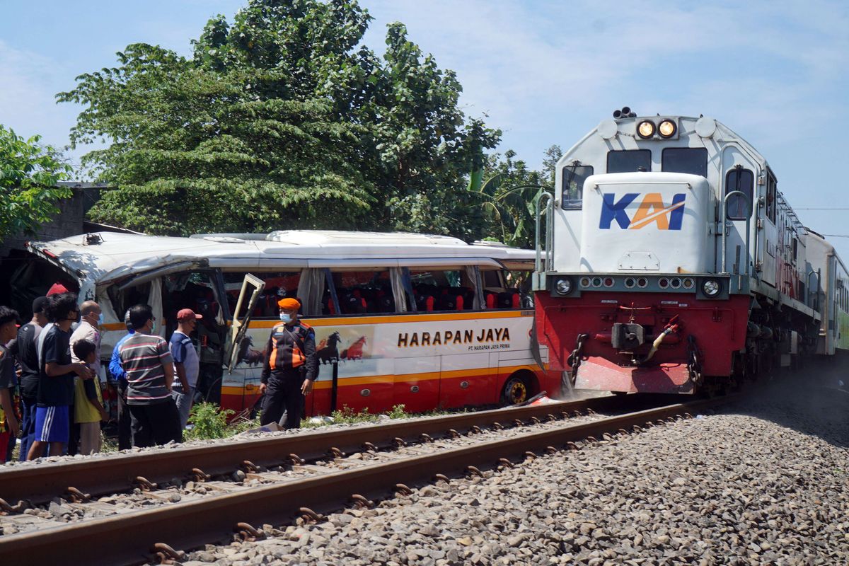 Kereta api melintas dekat bangkai bus pariwisata PO Harapan Jaya yang tertabrak KA Rapih Doho di perlintasan kereta api tanpa palang pintu di Desa Ketanon, Tulungagung, Jawa Timur, Minggu (27/2/2022). Kecelakaan yang terjadi sekitar pukul 05.00 WIB itu menyebabkan lima dari 43 penumpang termasuk awak bus meninggal dunia dan 14 lainnya luka-luka dan harus dilarikan ke RSUD dr. Iskak Tulungagung untuk mendapat pertolongan kedaruratan medis.