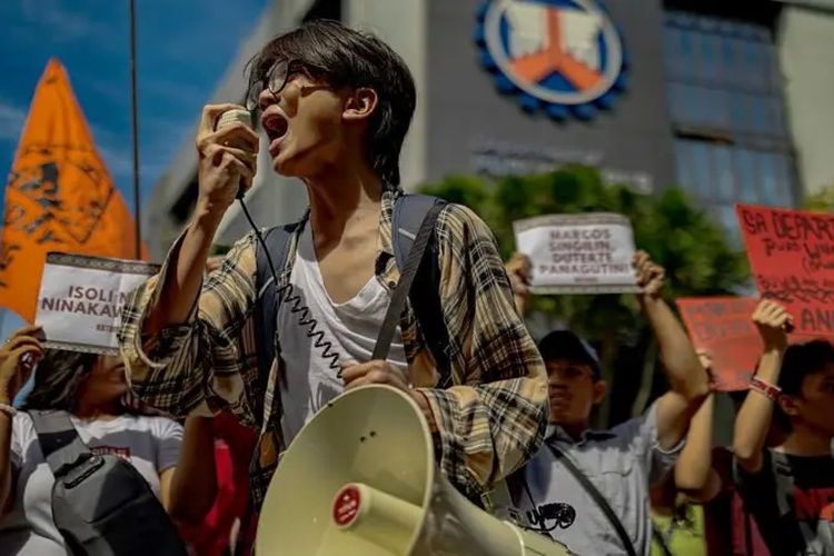 Seorang demonstran berusia muda berbicara lewat megafon di depan massa pengunjuk rasa.