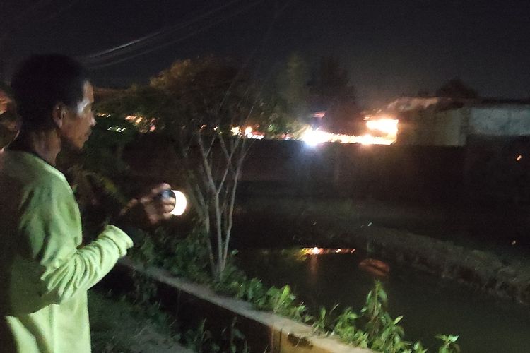 Sugiman (50) warga Desa Ngelo Wetan, Kecamatan Mijen, Kabupaten Demak berjaga di tepian sawah memantau air luapan sungai yang mulai menggenangi wilayah setempat, Senin (12/2/2024) malam. (KOMPAS.COM/NUR ZAIDI