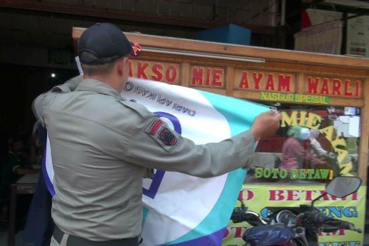 Petugas satpol PP memasang spanduk untuk menutupi warung makan yang buka pada siang hari di Duren Sawit, Senin (13/5/2019).