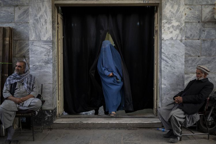 Seorang wanita Afghanistan meninggalkan rumah ibadah Syiah di lingkungan yang didominasi Hazara sementara dua pria berjaga di Kabul, Afghanistan, Selasa, 9 November 2021.