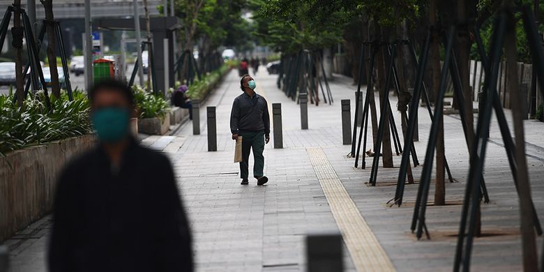 Pejalan kaki melintas di trotoar Jalan Jenderal Sudirman, Jakarta, Selasa (7/4/2020). Pemerintah telah resmi menetapkan Pembatasan Sosial Berskala Besar (PSBB) di wilayah DKI Jakarta dalam rangka percepatan penanganan COVID-19.