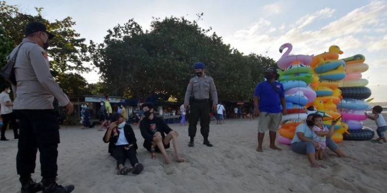 Anggota Polisi menegur warga yang beraktivitas di area pantai saat pelaksanaan Pemberlakuan Pembatasan Kegiatan Masyarakat (PPKM) Darurat di Pantai Sanur, Denpasar, Bali, Sabtu (03/07).