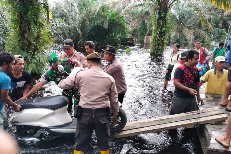 Anggota Polsek Pangkalan Kerinci bersama TNI saat membantu menaikkan motor warga ke atas pompong untuk melewati jalan yang banjir, di Kelurahan Kerinci Kota, Kecamatan Pangkalan Kerinci, Kabupaten Pelalawan, Riau, Senin (8/1/2024).