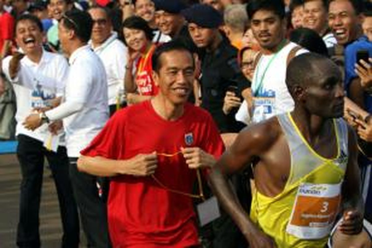 Gubernur DKI Jakarta Joko Widodo mengejar pelari asal Kenya, Stephen Tum, untuk mengalungkan tanda pemenang pada Mandiri Jakarta Marathon 2013, di kawasan Monas Jakarta Pusat, Minggu (27/10/2013). Selain nomor maraton 42 km, dilombakan pula setengah maraton (21 km), 10 km, dan 5 km. Acara tersebut diikuti sekitar 10.000 pelari elite nasional dan internasional untuk memperebutkan total hadiah Rp 2,5 miliar.