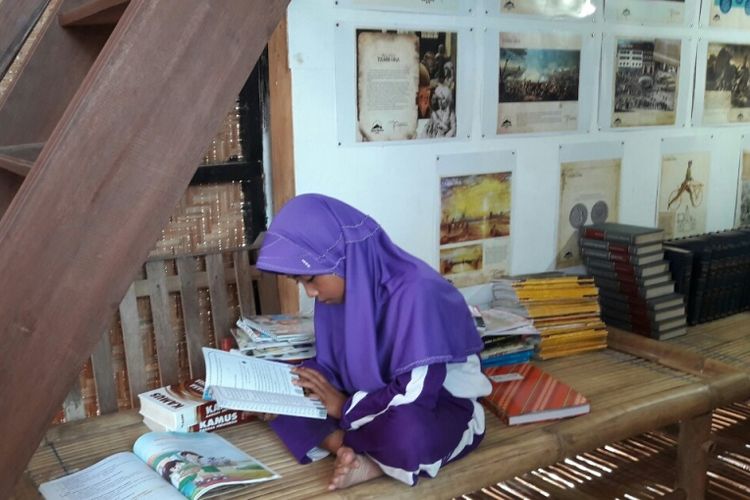 Seorang anak sangat serius membaca buku di Nusa Pustaka.