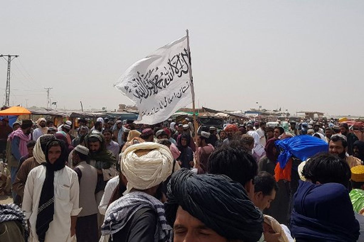 Orang-orang berkumpul di sekitar bendera Taliban saat mereka menunggu kerabat dibebaskan dari penjara di Afghanistan menyusul 'amnesti' oleh Taliban, dekat titik perbatasan Pakistan-Afghanistan di Chaman pada 17 Agustus 2021.