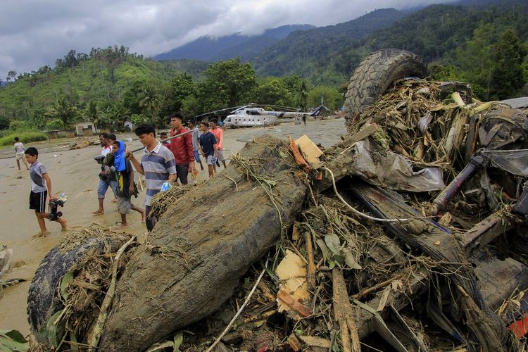 Sejumlah warga melintasi sebuah mobil yang terbalik akibat banjir bandang di Sentani, Kabupaten Jayapura, Papua, Minggu (17/3/2019). Berdasarkan data BNPB, banjir bandang yang terjadi pada Sabtu (16/3) tersebut mengakibatkan 42 tewas. 