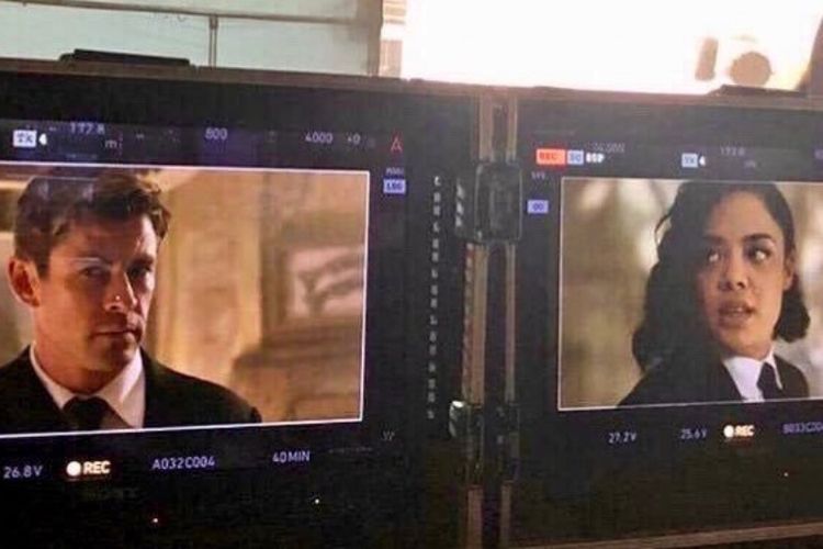 Chris Hemsworth dan Tessa Thompson tampak dalam monitor sebagai Agen H dan Em dalam Men in Black.