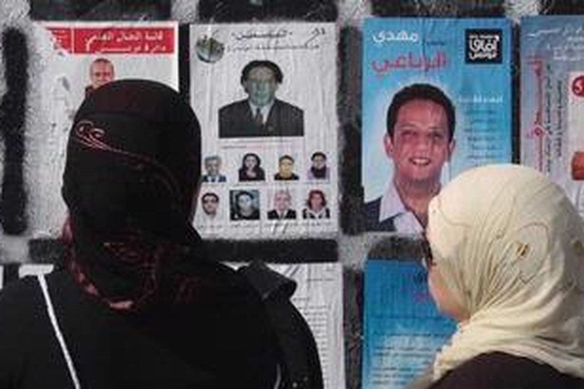 Dua warga Tunisian melihat poster para calon anggota dewan konstitusi di Tunis, Sabtu (22/10/2011) atau sehari menjelang pemilu pertama pascapemberontakan yang menumbangkan Presiden Ben Ali.