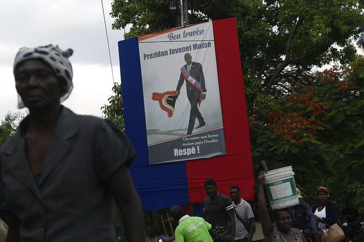 People walk near a poster featuring President Jovenel Moise in Port-au-Prince, Haiti, Saturday, July 17, 2021, ten days after Moise was assassinated in his home on July 7. (AP Photo/Matias Delacroix)