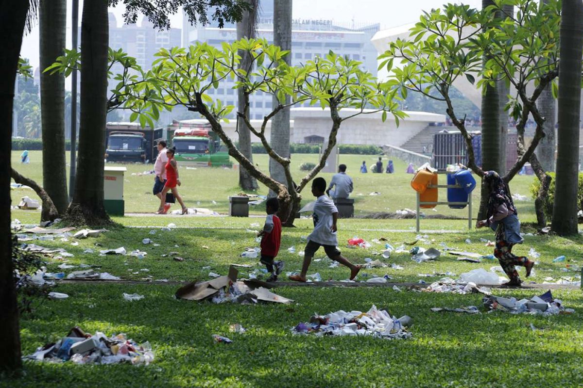 Pengunjung melntas di antara sampah yang masih berserakan di kawasan Monumen Nasional, Jakarta, Minggu (29/4/2018). Sampah yang berserakan merupakan sisa dari acara pembagian sembako yang berlangsung pada Sabtu (28/4/2018) di lokasi tersebut.