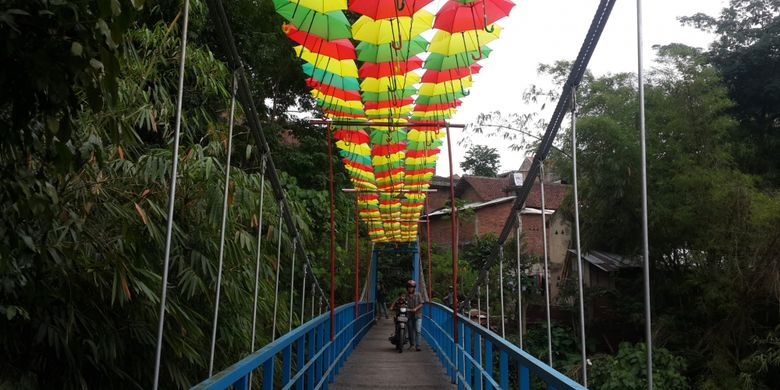 Seorang pengendara saat melintas di atas jembatan gantung di RT 6 RW 5 Kelurahan Penanggungan, Kecamatan Klojen, Kota Malang, Jawa Timur, Selasa (14/11/2017). Jembatan itu dihias dengan payung supaya kelihatan lebih indah.