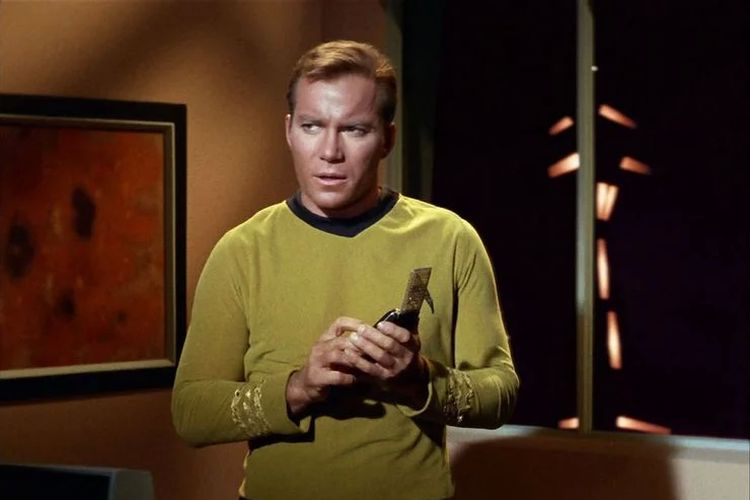 Tokoh Captain Kirk di film Star Trek sedang menggenggam sebuha komunikator yang konon menjadi inspirasi Cooper mencipatkan ponsel genggam.