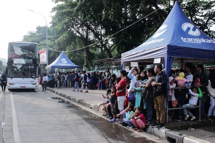 Masyarakat mengantre saat menaiki bus wisata di kawasan Monumen Nasional, Gambir, Jakarta Pusat, Minggu (29/12/2019). Bus wisata dimanfaatkan masyarakat untuk berkeliling ibukota bersama keluarga secara gratis.
