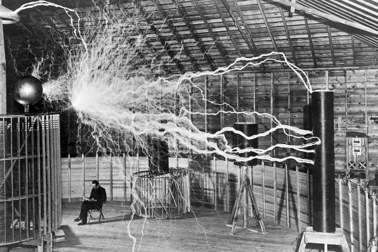 Nikola Tesla duduk saat sedang mengamati temuannya yaitu Tesla coil