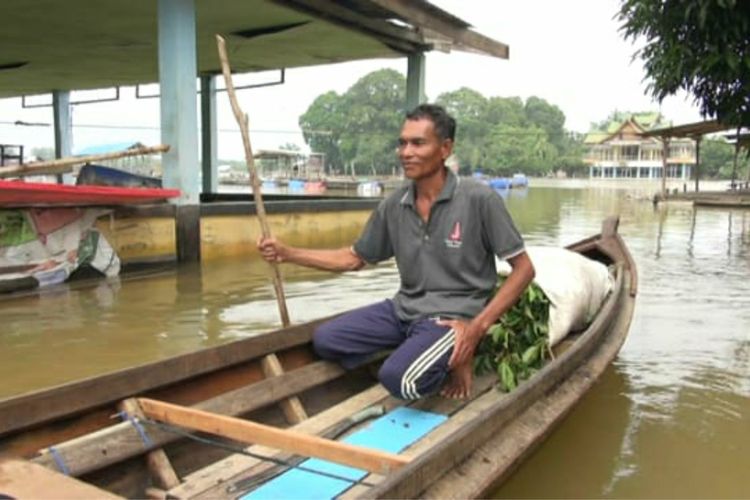 Sarial (52) warga Desa Buluh Cina, Kecamatan Siak Hulu, Kabupaten Kampar, Riau, membawa makanan untuk ternak kambing menggunakan perahu, Kamis (19/12/2019). Tujuh ekor kambing milik Sarial nyaris mati tenggelam akibat banjir.