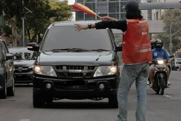 Ilustrasi juru parkir yang menggunakan bendera tangan sebagai alat bantu isyarat pemberi arahan parkir.