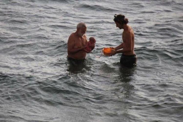 Seorang pria yang kemungkinan adalah seorang dokter membawa seorang bayi yang dilahirkan di Laut Merah, Mesir.