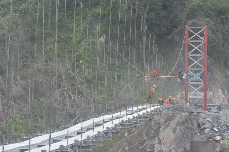 Sejumlah pekerja menyelesaikan pembangunan jembatan gantung Gladak Perak di Lumajang, Jawa Timur, Sabtu (9/4/2022). Kementerian Pekerjaan Umum dan Perumahan Rakyat membangun jembatan gantung darurat tersebut untuk dilewati sementara oleh kendaraan roda dua, sebelum jembatan permanen yang rusak akibat awan panas guguran Gunung Semeru kembali dibangun.