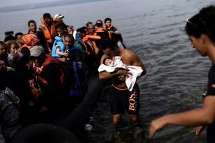 Seorang pria mencium seorang bayi saat dia menolong pengungsi dan migran yang terdampar di pulau Lesbos, Yunani, setelah berhasil menyeberangi laut Aegean dari Turki, 26 September 2015.